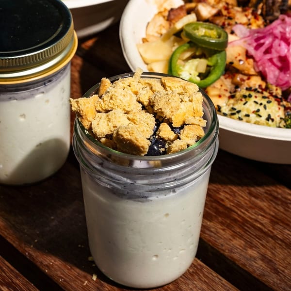 Yogurt parfait with crumble topping and blueberries in a glass jar, with other food bowls in the background.