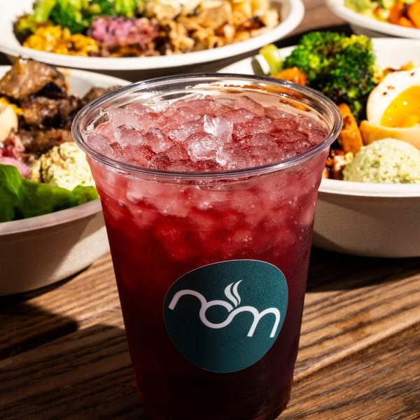 Iced red drink with a logo on a wooden table, surrounded by several bowls of colorful food.